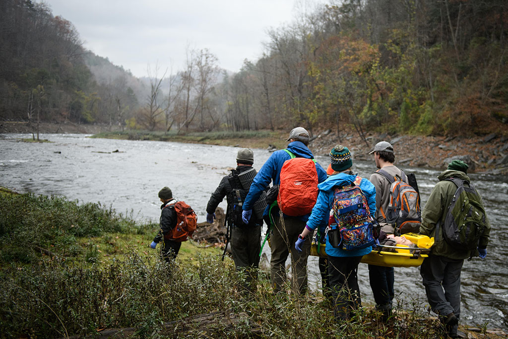 SOLO students carry a patient on a backboard by a river